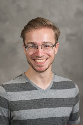 Picture of a man wearing glasses wearing a striped gray shirt with a gray background.